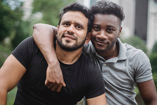 two multicultural men looking at the camera and smiling with their arms around each other