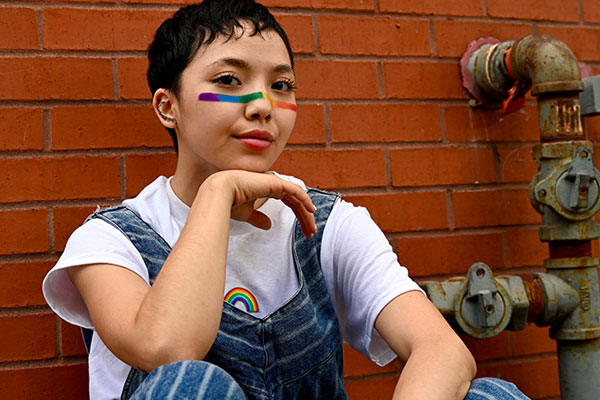 woman sitting by brick wall with rainbow paint on her face