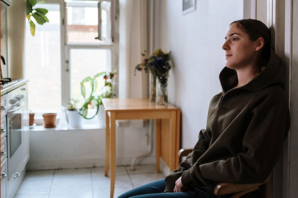 woman in a hoodie sitting in a kitchen while staring and thinking