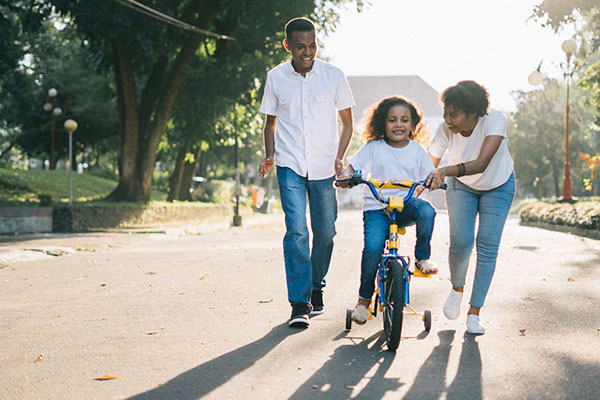 black family helping their young daughter learn to ride a bike