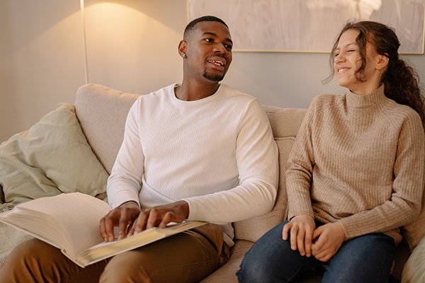 man in a white sweater sitting on the couch reading in Braille