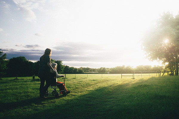elderly woman being pushed in a wheelchair in a field with the sun shining