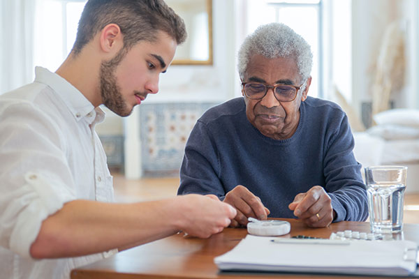 elderly man in blue shirt with practitioner in white shirt helping with medication
