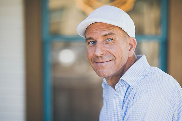 man with white cap and blue checked shirt sitting down