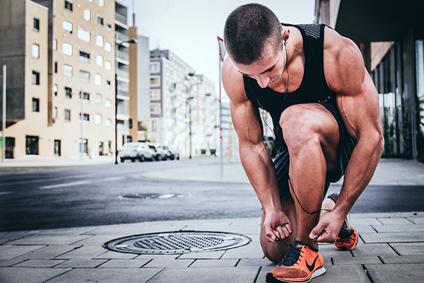 young muscular man tying his shoes while running