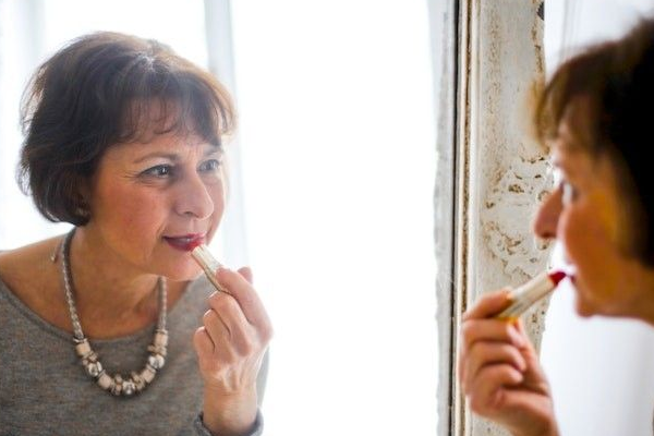 older woman applying lipstick in front of the mirror